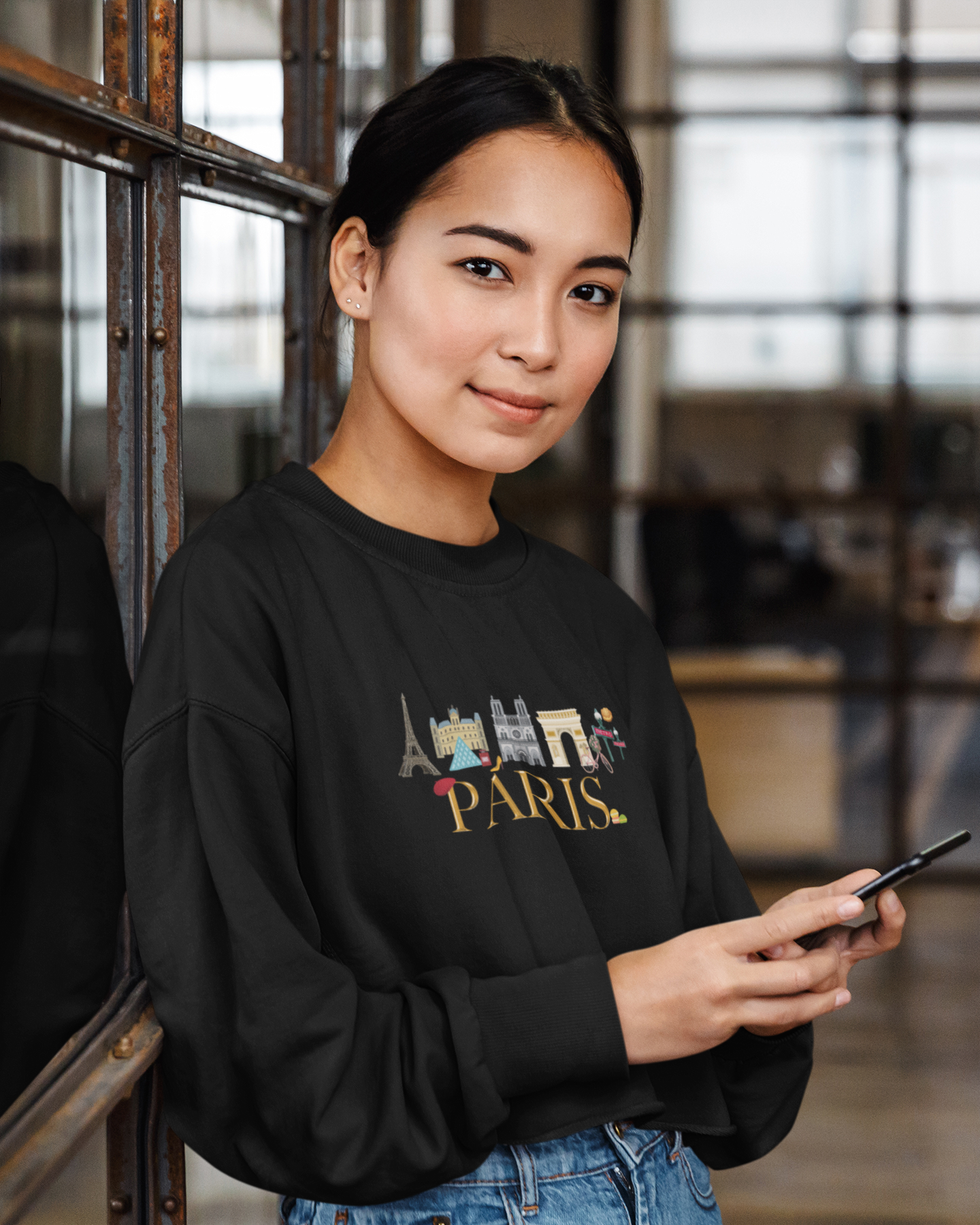 woman-in-a-cropped-sweatshirt-featuring-a-graphic-design-of-the-word-paris-and-iconic-symbols-of-France-holding-a-phone